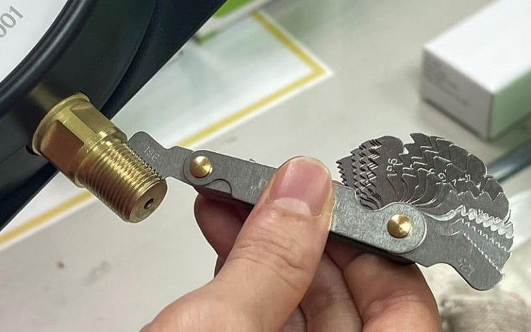 Technician checking instrument fitting thread pitch with a thread gauge